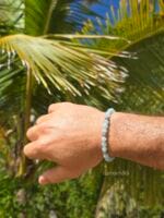 Bracciale in pietre naturali di acquamarina con elementi in argento 925, indossato al polso da un uomo in un contesto tropicale con palme.