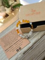 Bracciale con pietre naturali di ambra e labradorite bianca appoggiato sulla sua confezione regalo in cartone ecologico con il logo Namamala e foglietto informativo.