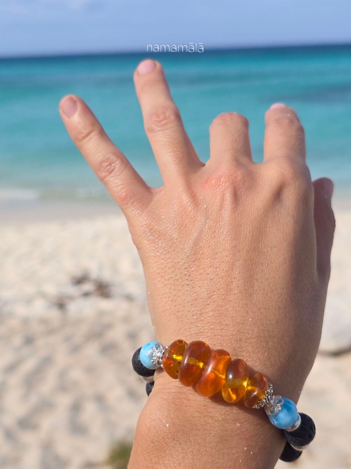 bracciale ambra larimar lava indossato al polso di donna in spiaggia con lo sfondo del mare azzurro e il cielo