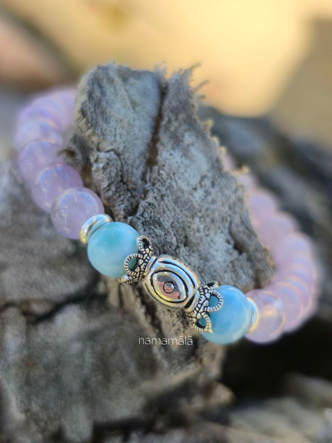 bracciale di ametista e larimar con perla centrale in argento 925, appoggiato su un pezzo di legno marino.