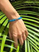 Bracciale in Apatite blu naturale e argento 925 indossato al polso di donna su uno sfondo di grandi foglie di palma. verde.