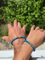 Coppia di bracciali in pietre naturali di Apatite blu con centrale perla in argento 925 indossati al polso da un uomo e una donna su sfondo naturale di foglie verdi.