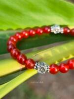 Dettaglio ravvicinato della perla in argento 925 del bracciale in corniola rossa appoggiato a una foglia verde.