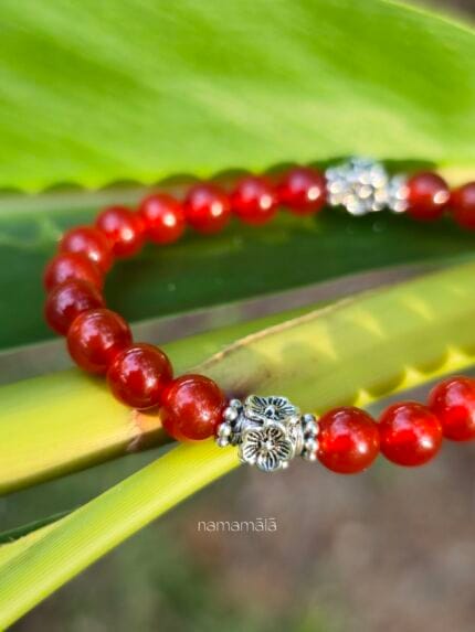 Dettaglio ravvicinato della perla in argento 925 del bracciale in corniola rossa appoggiato a una foglia verde.