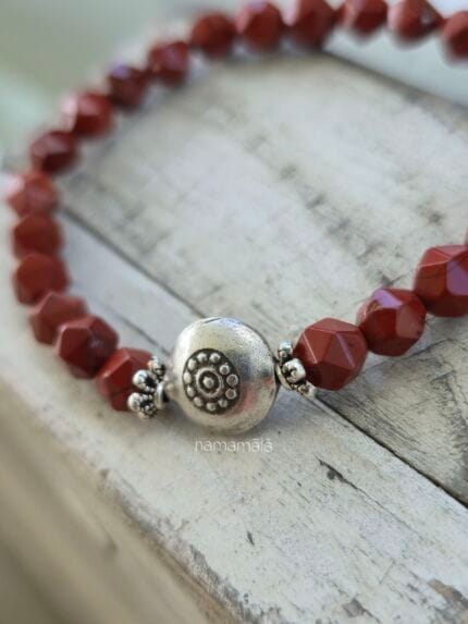 Dettaglio ravvicinato della perla in argento karen del bracciale diaspro rosso su uno sfondo legnoso.