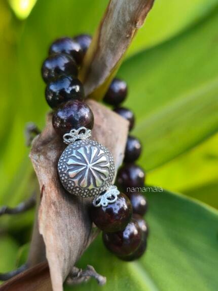 Dettaglio ravvicinato del bracciale "Ricomincio da me" in pietre naturali di Granato almandino con elemento centrale perla in argento Karen Tribe 97-99%. con uno sfondo naturale di foglie verdi.