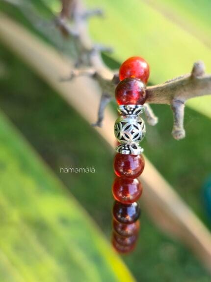 Dettaglio macro di un bracciale in granato spessartite naturale arancio brillante con distanziatore centrale in argento traforato, fotografato all'aperto con luce naturale.