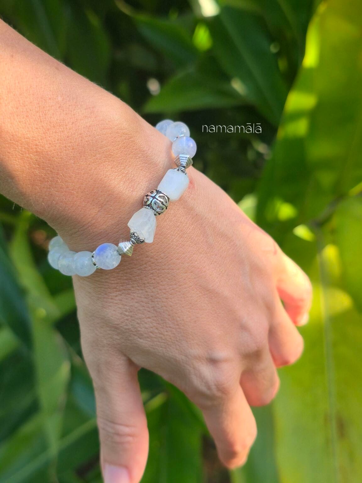 Bracciale in labradorite bianca con elementi in argento 925. E' indossato al polso di donna con uno sfondo di natura verde,