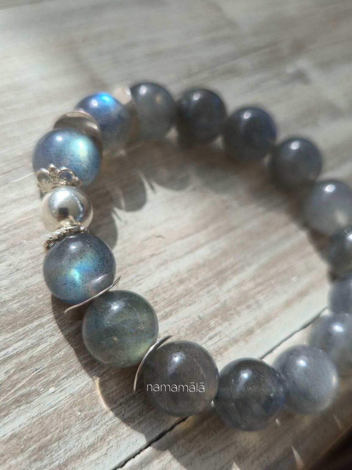 Pietre ravvicinate del bracciale labradorite dove si mostrano i riflessi cangianti della pietra, appoggiata su un ripiano in legno chiaro e sotto la luce del sole.