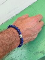 Bracciale "Nel Blu dipinto di Blu" realizzato con pietre naturali di Lapislazzuli blu intenso, indossato al polso da un uomo, con perla centrale e distanziatori in argento Karen Tribe puro al 97-99%