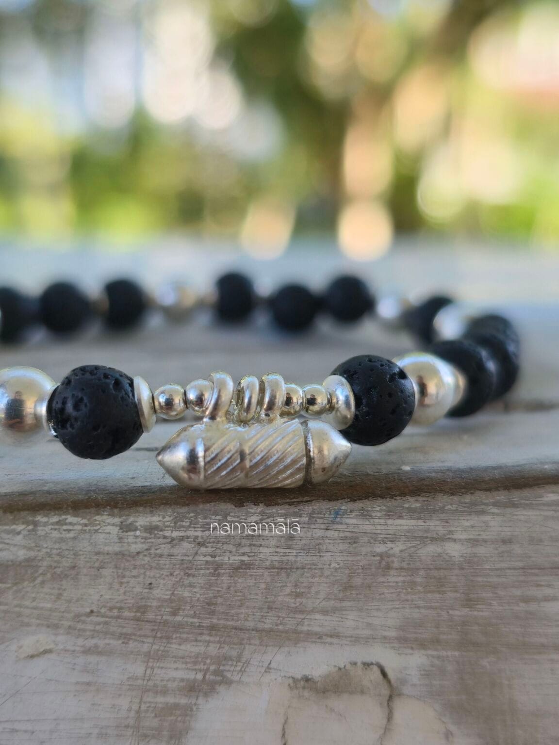 Bracciale con lava naturale e ciondolo in argento 925 contenente un foglietto con scritto "Io Esisto" e poi chiuso in sicurezza. E indossato al polso di donna come esempio.