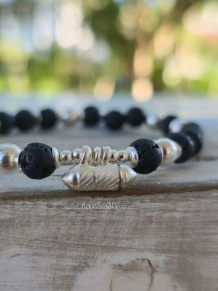 Bracciale con lava naturale e ciondolo in argento 925 contenente un foglietto con scritto "Io Esisto" e poi chiuso in sicurezza. E indossato al polso di donna come esempio.