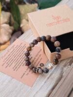 Bracciale con pietre naturali di Pietersite e vicino la sua confezione regalo in cartone ecologico con il logo Namamala e foglietto informativo.