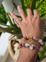 Due bracciali in pietre naturali di quarzo ematoide con venature rosse e arancio, mostrati nelle due versioni con charm e distanziatori in argento 925 e in argento con la placcatura oro, indossati al polso di donna insieme.