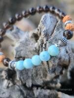 bracciale con pietre di larimar e quarzo fumè e semi di rudraksha appoggiato ad un tronco