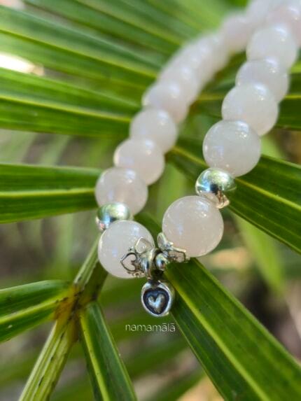 Dettaglio di un bracciale in Quarzo Rosa naturale con perle tonde e piccolo ciondolo a cuore in argento 925 su una foglia verde.