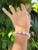 Bracciale in quarzo rosa con simbolo centrale piccolo cuore in argento 925. E' indossato al polso di donna con uno sfondo di palme. Questa è una pietra per eccellenza del quarto chakra.