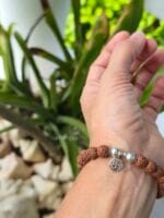 Bracciale con sacri semi indiani di rudraksha naturali e ciondolo simbolo om in argento 925, indossato al polso.