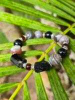 bracciale in tormalina nera sia a sfere che grezza, agata del botswana e perle di ambra, appoggiato su una foglia di palma verde.