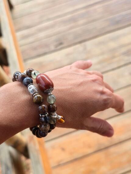 Set di bracciali in pietre naturali: Nuova Energia (tutto di Pietersite), Storm & Sun (Pietersite, Prehnite e Ambra baltica) indossato al polso di donna con sfondo pavimento in legno