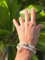 Set di bracciali in pietre naturali: Labradorite bianca e Ambra baltica e tutto Labradorite indossato su un polso di donna con lo sfondo delle piante verdi illuminate dal sole