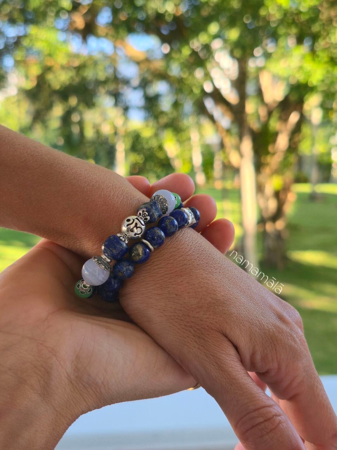 Bracciali yoga da uomo e da donna con pietre naturali di Lapislazzuli e lapislazzuli calcedonio blu e crisoprasio con distanziatori in argento 925, indossati al polso con un contesto di natura e foglie verdi illuminate dal sole.