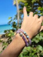 Set di ispirazione con bracciali in pietre naturali: Ajna in Ametista, Ametista e Larimar indossati al polso di una donna con uno sfondo la natura con alberi e in fondo il mare
